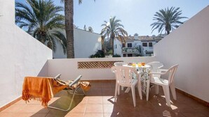 A sunlit patio with a table and chairs, a lounge chair, and a view of palm trees and buildings in the background. - Apartment Sol de Denia. Wifi, A/C (Dénia)
