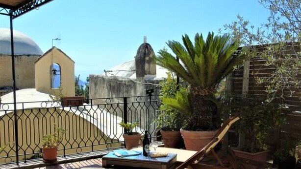 Terraço com espreguiçadeira, plantas em vasos e vista para uma igreja e cúpula.