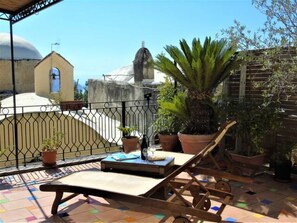 A terrace with a lounge chair, potted plants, and a view of a church and dome. - Casa Alma (Positano)