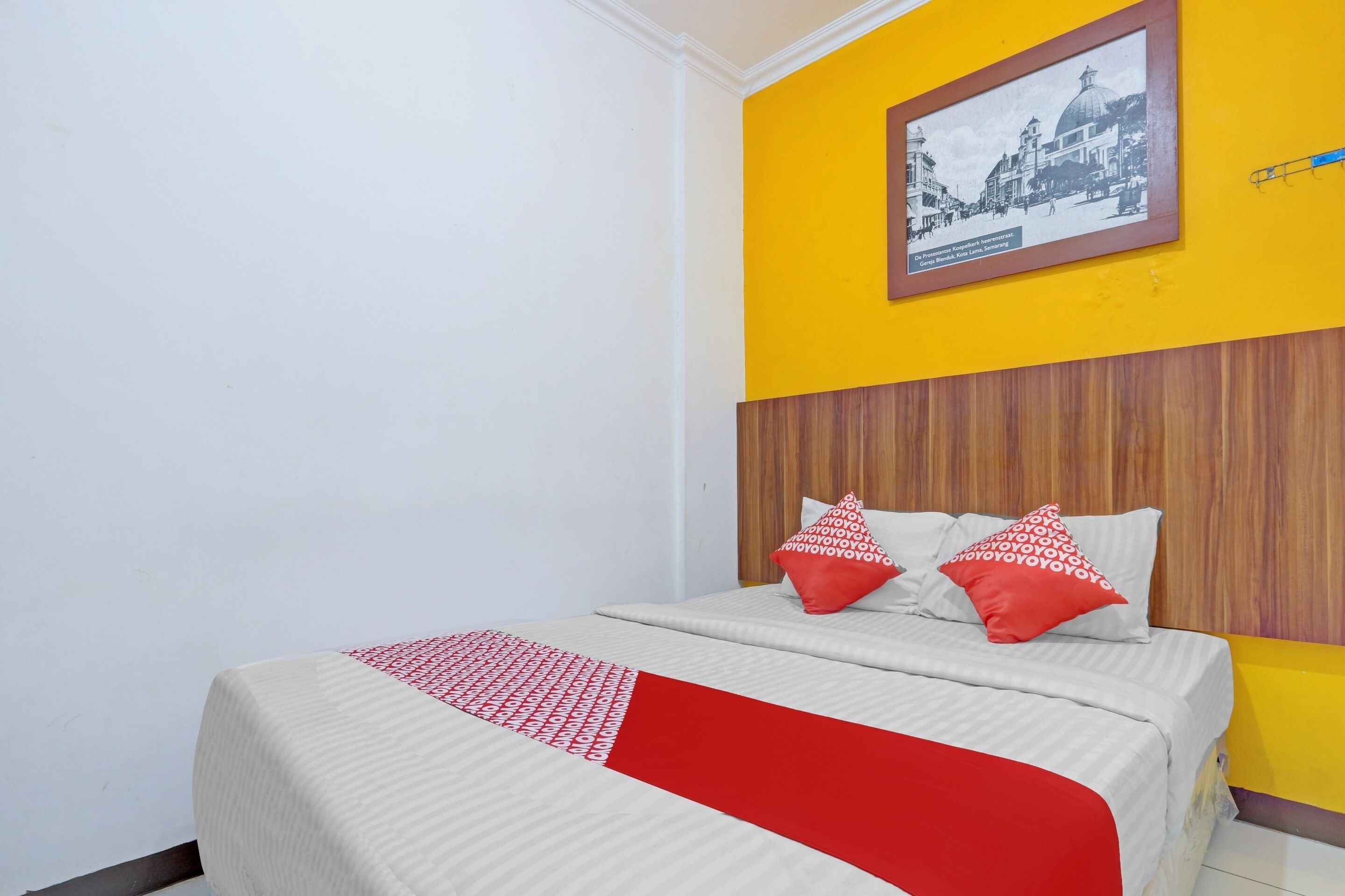 Ein Hotelzimmer mit einem Bett, zwei roten Kissen, einem gerahmten Bild an der Wand und einer gelben Akzentwand.