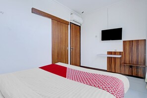 Une chambre avec un lit, une armoire, une télévision et une petite étagère.