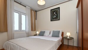 Un dormitorio con una cama grande, dos mesitas de noche con lámparas, una ventana con cortinas, un radiador y una obra de arte enmarcada en la pared.