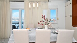 Un comedor con una mesa dispuesta para cuatro, un jarrón con flores y vista al mar a través de amplios ventanales.