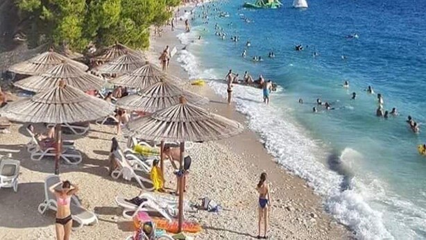 Una playa con sombrillas, gente y cielo despejado.