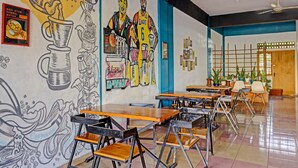Un café avec des tables et des chaises, une fresque murale et un ventilateur au plafond.