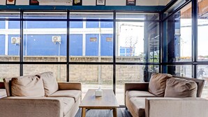 Un intérieur moderne avec deux canapés beige, une table basse en bois et de grandes fenêtres donnant sur un immeuble bleu et un mur de briques.