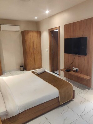 Habitación de hotel con cama, armario de madera, televisor montado en la pared y una pequeña estantería con el control remoto.