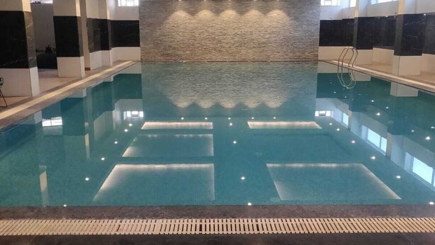 Una piscina interior con una pared de azulejos al fondo y suelo de madera.