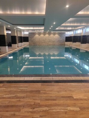 Ein Hallenbad mit einer befliessten Wand im Hintergrund und Holzboden.