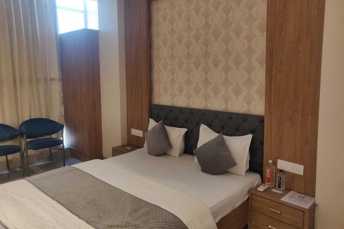 Una habitación de hotel con una cama grande, un cabecero de diseño geométrico, una mesita de noche con una botella de agua y una silla junto a la ventana.