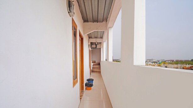 A narrow corridor with a tiled floor, a wooden door, and a window overlooking a construction site. - Hotel O Biring Residence (Wargasaluyu)