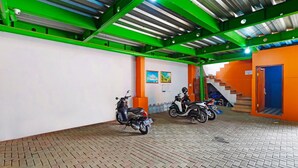 A covered parking area with scooters parked, a staircase, and a green metal ceiling. - Hotel O Biring Residence (Wargasaluyu)