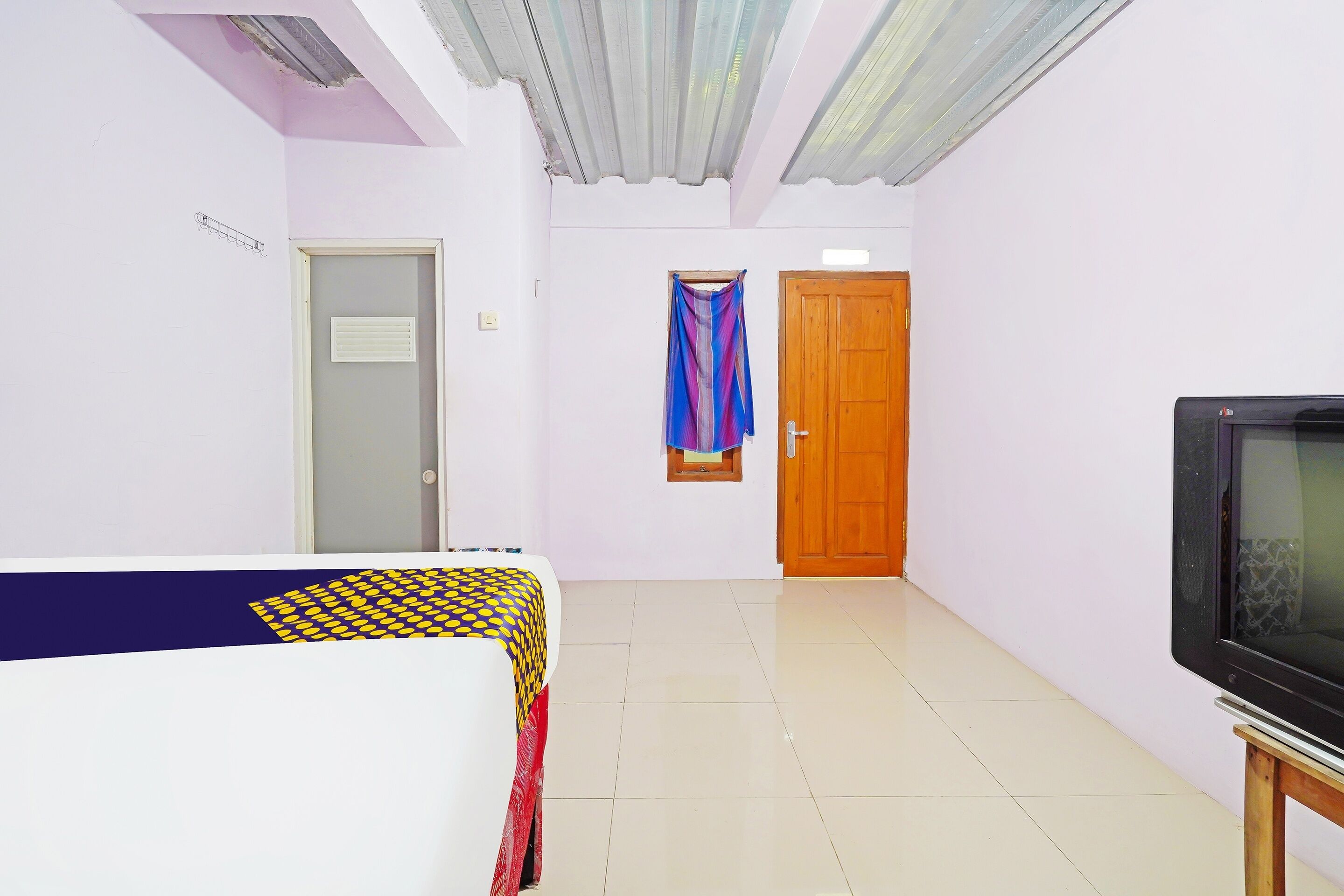 Una habitación con cama, televisor sobre un mueble, una puerta y una ventana con cortinas.