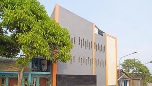 A modern building with a large grey facade, a metal gate, and a tree in front. - Hotel O Biring Residence (Wargasaluyu)