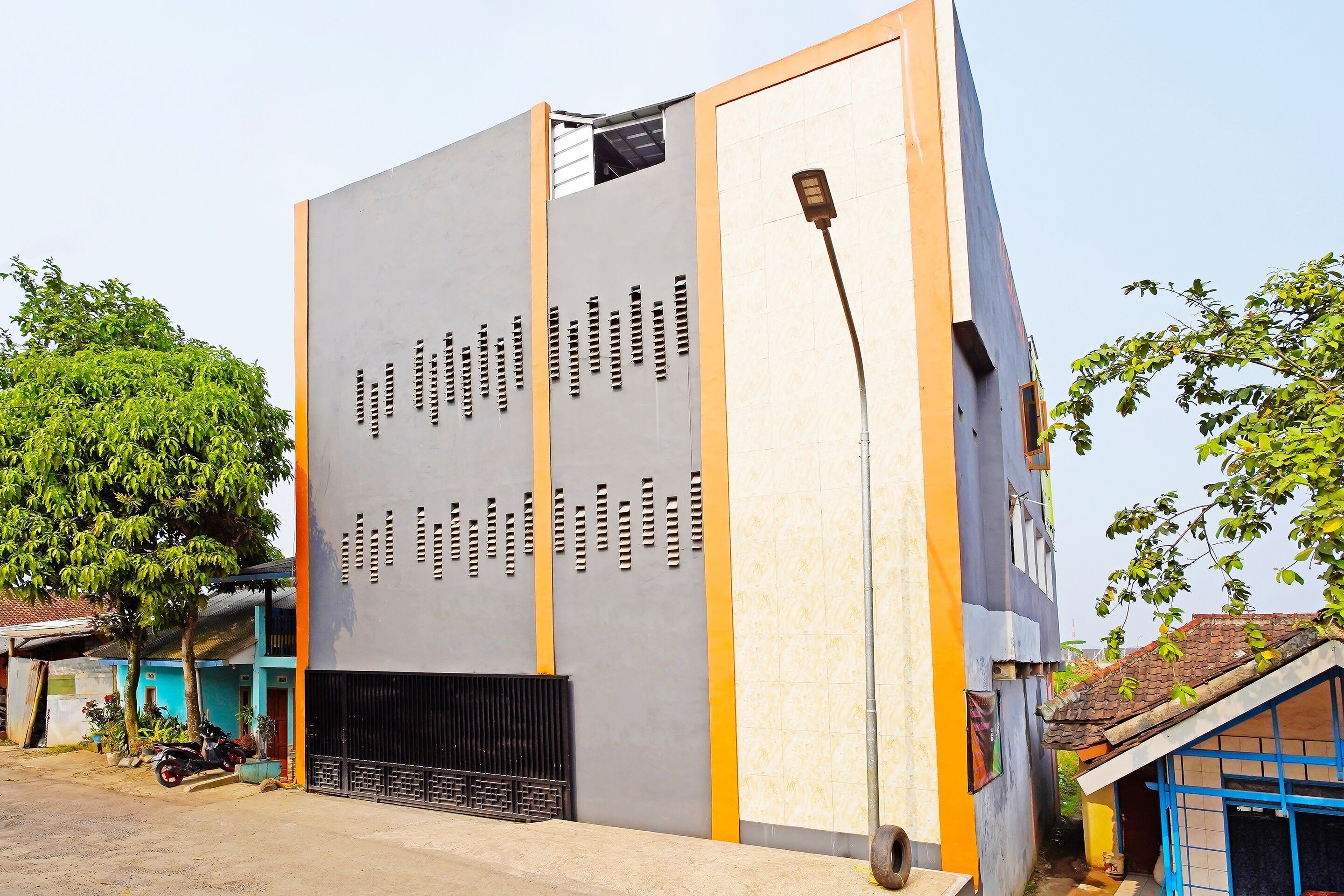 A modern building with a large vertical panel displaying text, a street lamp, and a tree.