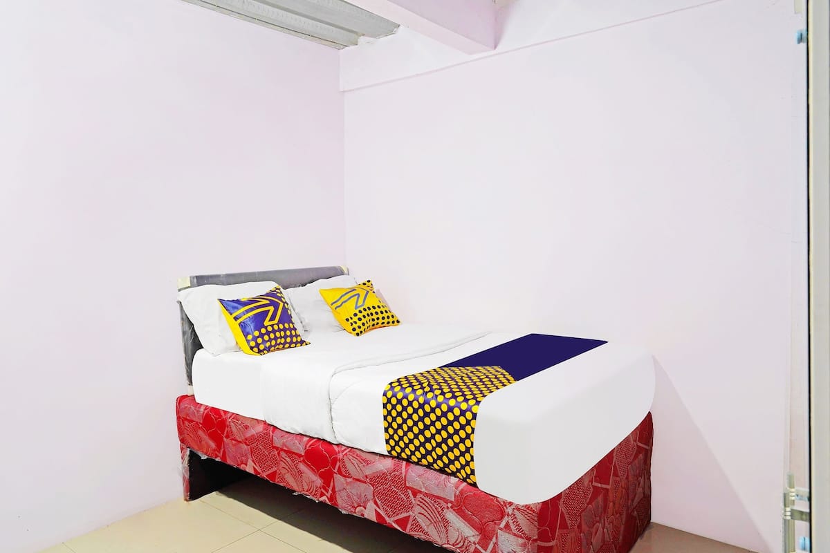 A bed with a white mattress, red and white patterned bed skirt, and two pillows with yellow and blue patterns.
