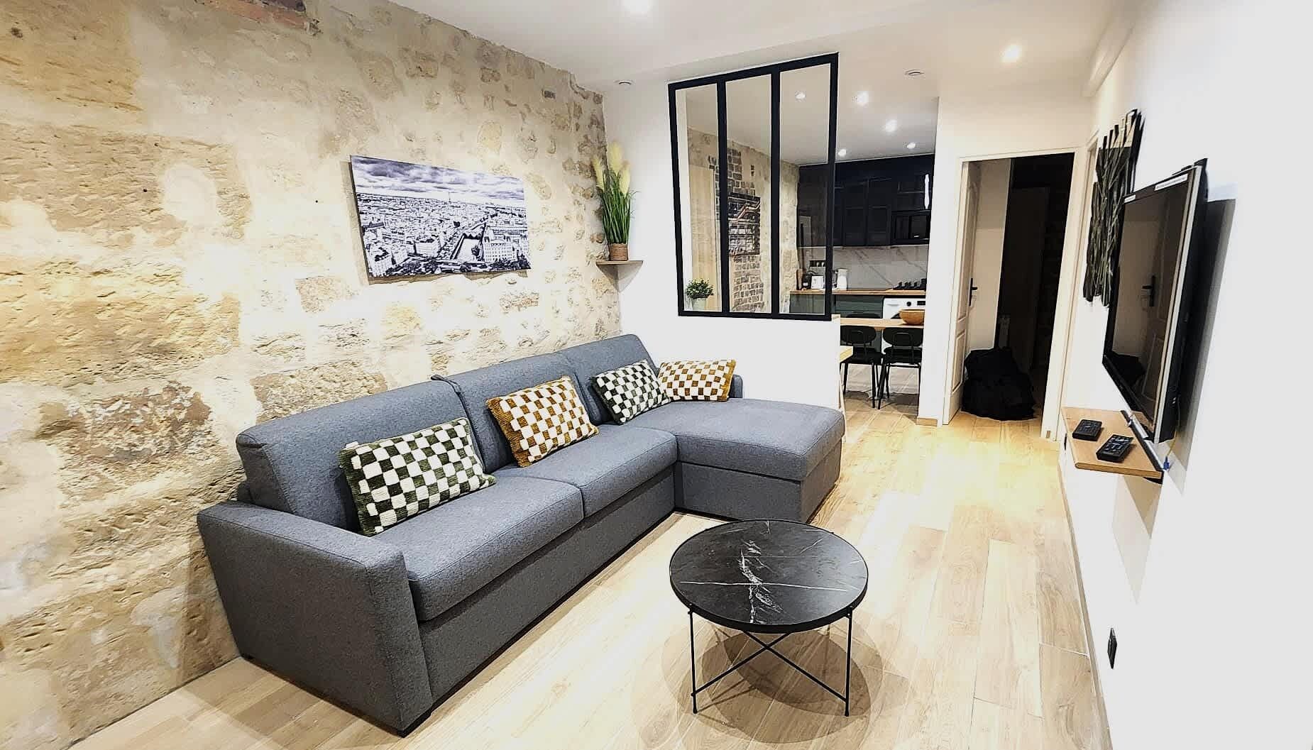 A modern living room with a grey sectional sofa, checkered cushions, a small black round table, and a large mirror.