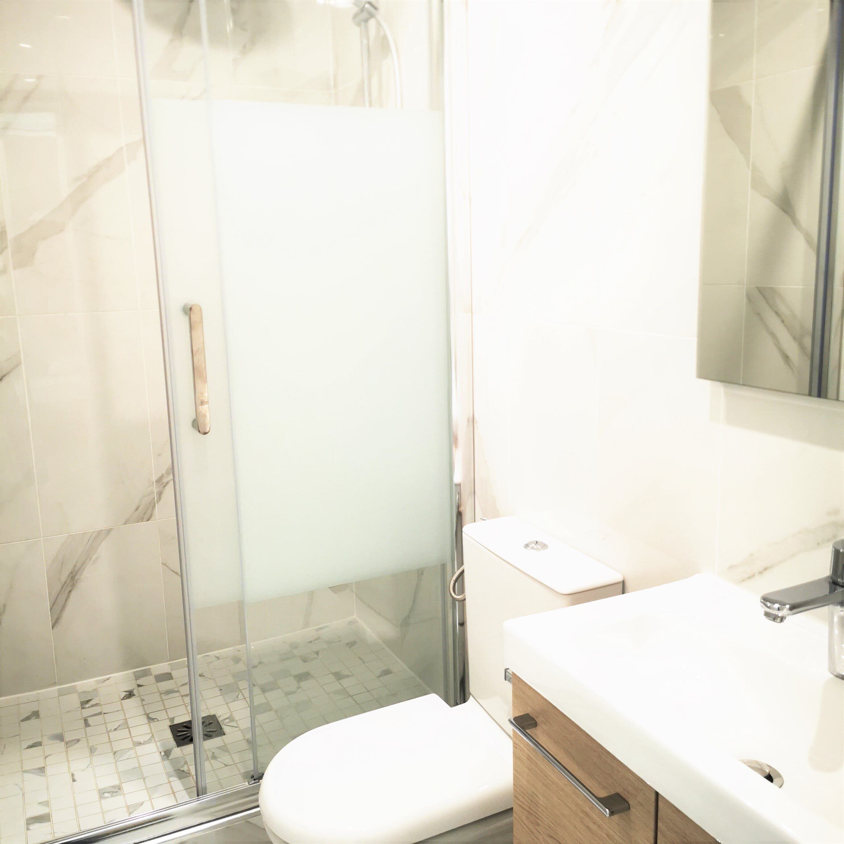 A modern bathroom with a glass shower enclosure, a white toilet, and a vanity with a mirror.