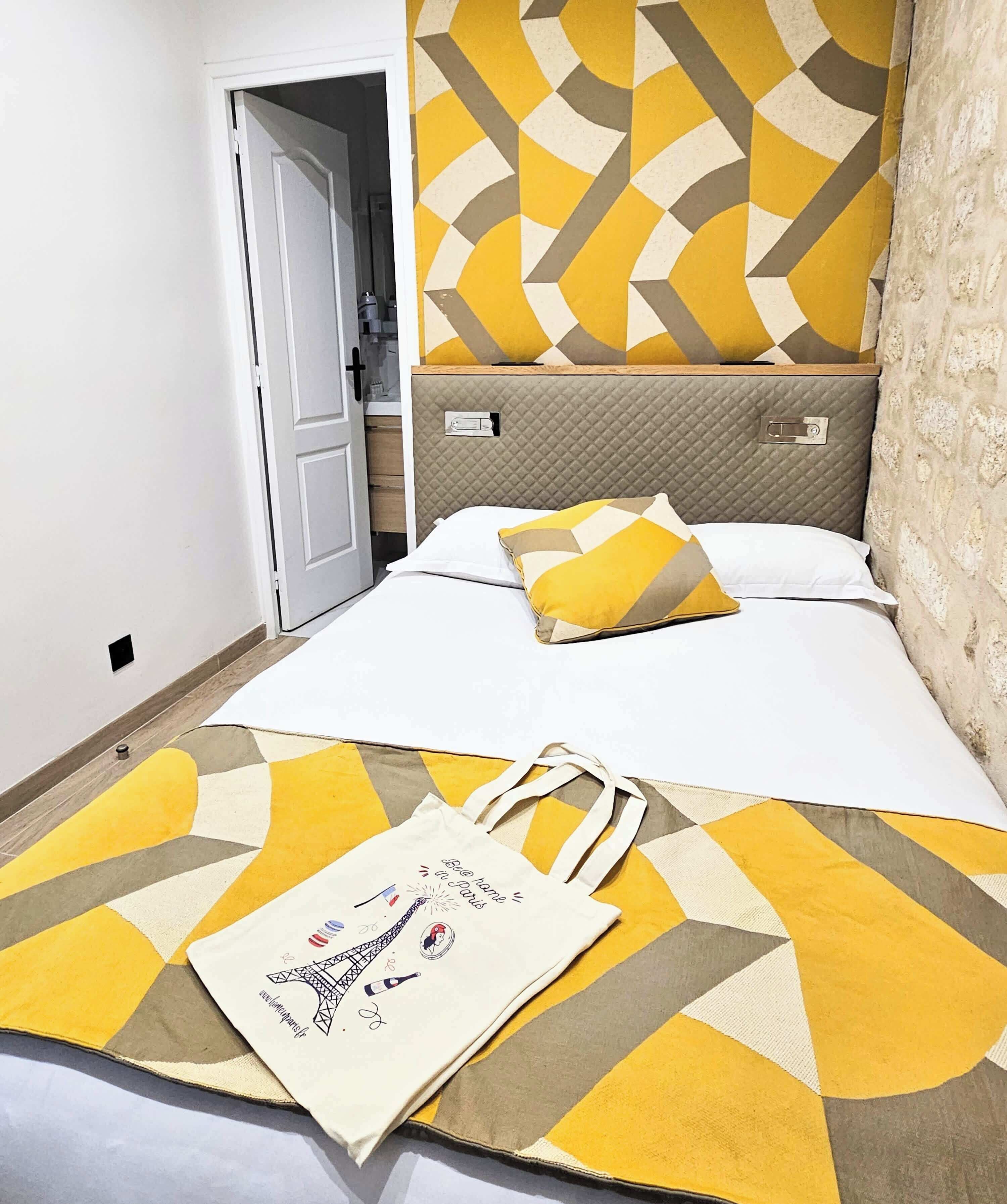 A hotel room with a bed, a nightstand, a wall with a geometric pattern, and a door leading to another room.