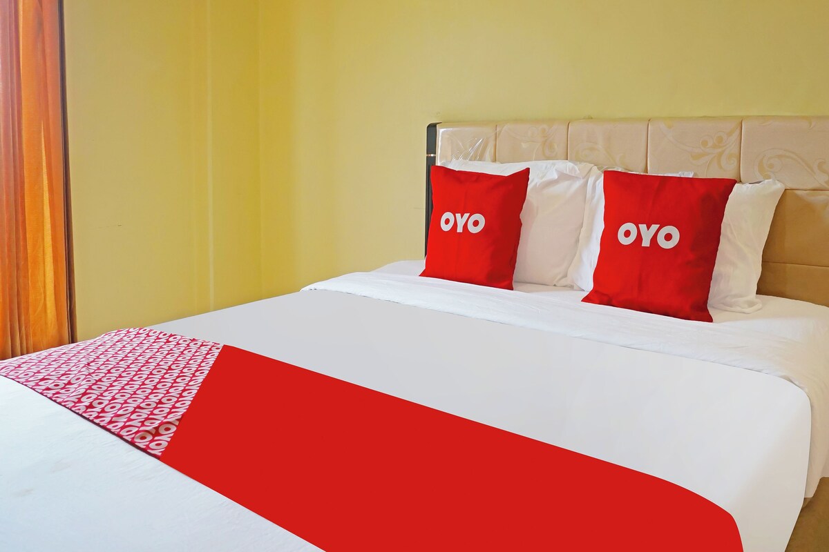 A bed with a white and red bedspread, two red pillows with the word 'OYO' on them, and a yellow wall.