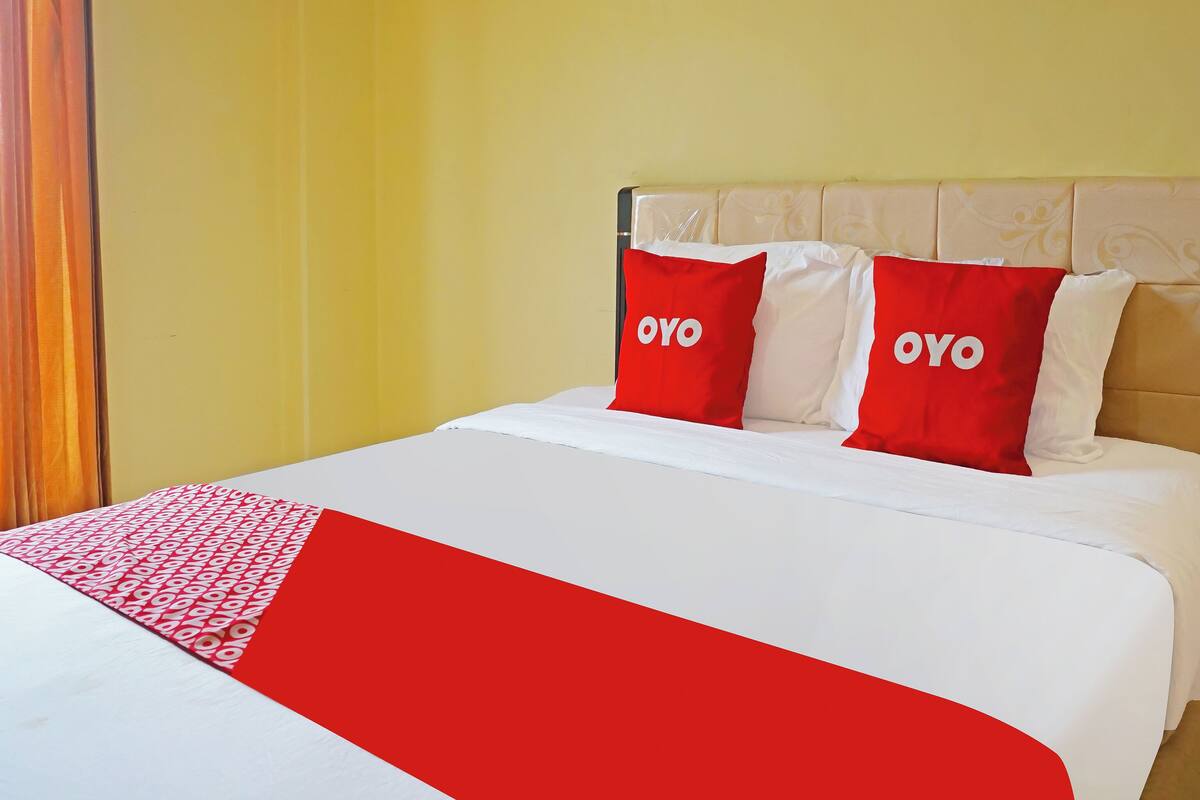 A bed with a white and red bedspread, two red pillows with the word 'OYO' on them, and a yellow wall.