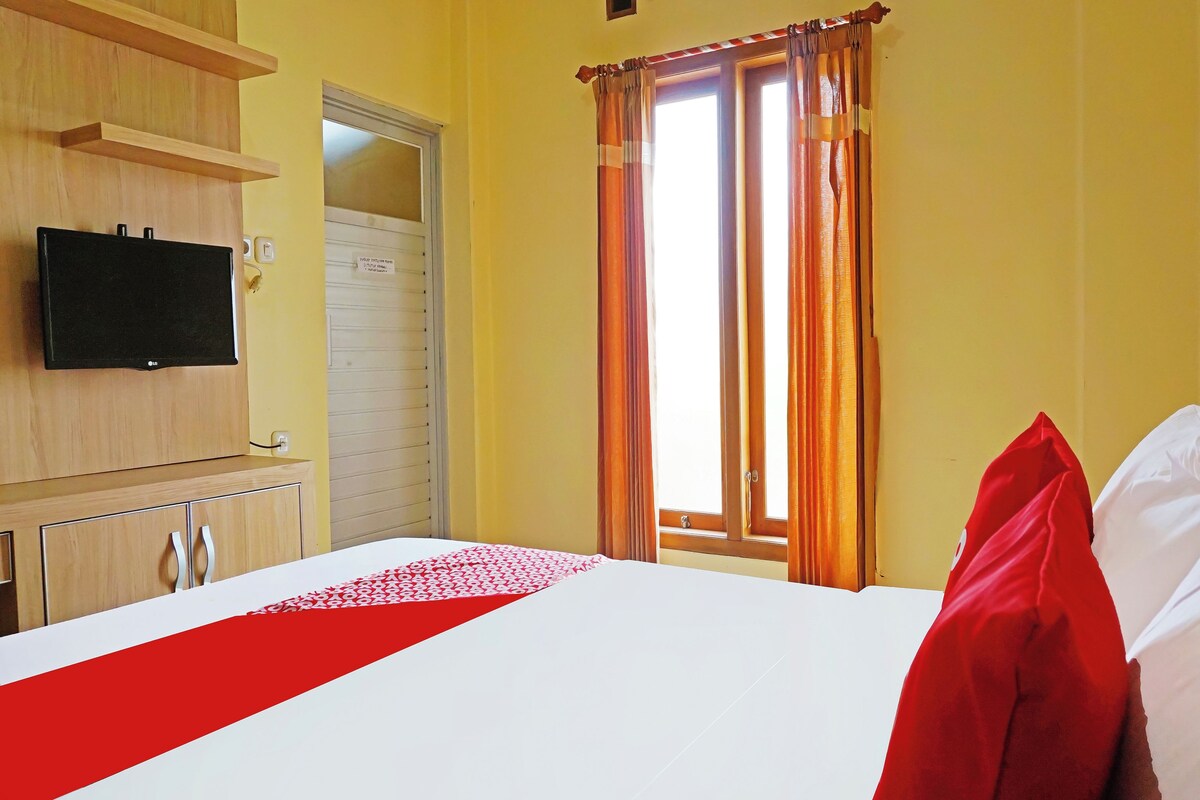 A hotel room with a bed, a TV mounted on the wall, a door, and a window with curtains.