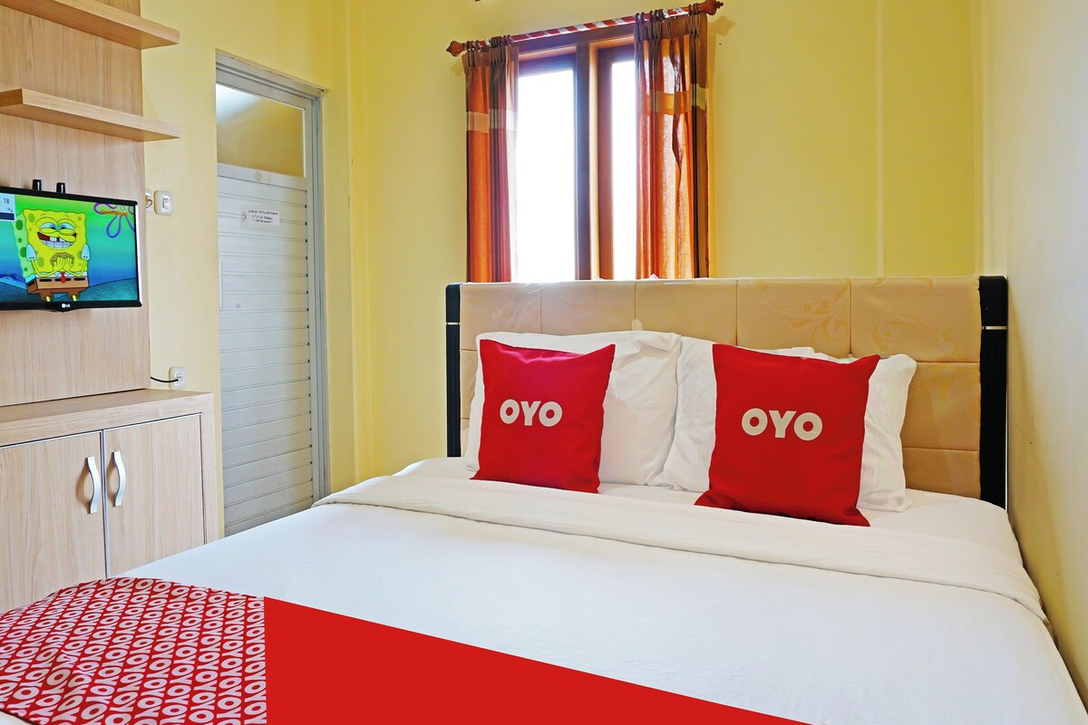 Habitación de hotel con cama, televisor en un mueble bajo y ventana con cortinas.