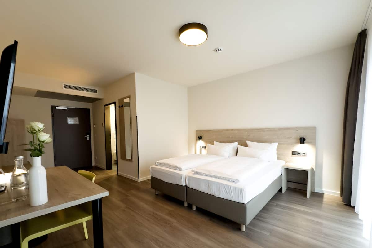 A hotel room with a double bed, bedside tables, a desk with a chair, a mirror, and a vase with flowers.