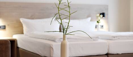 A bed with white linens, a bedside table with a vase containing a plant, and a nightstand with a lamp.