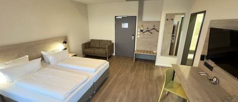 A hotel room with a bed, a desk, a chair, a TV, and a coat rack.