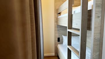 Una cama litera con listones de madera y ropa de cama blanca, suelo de madera y una puerta con cortina.