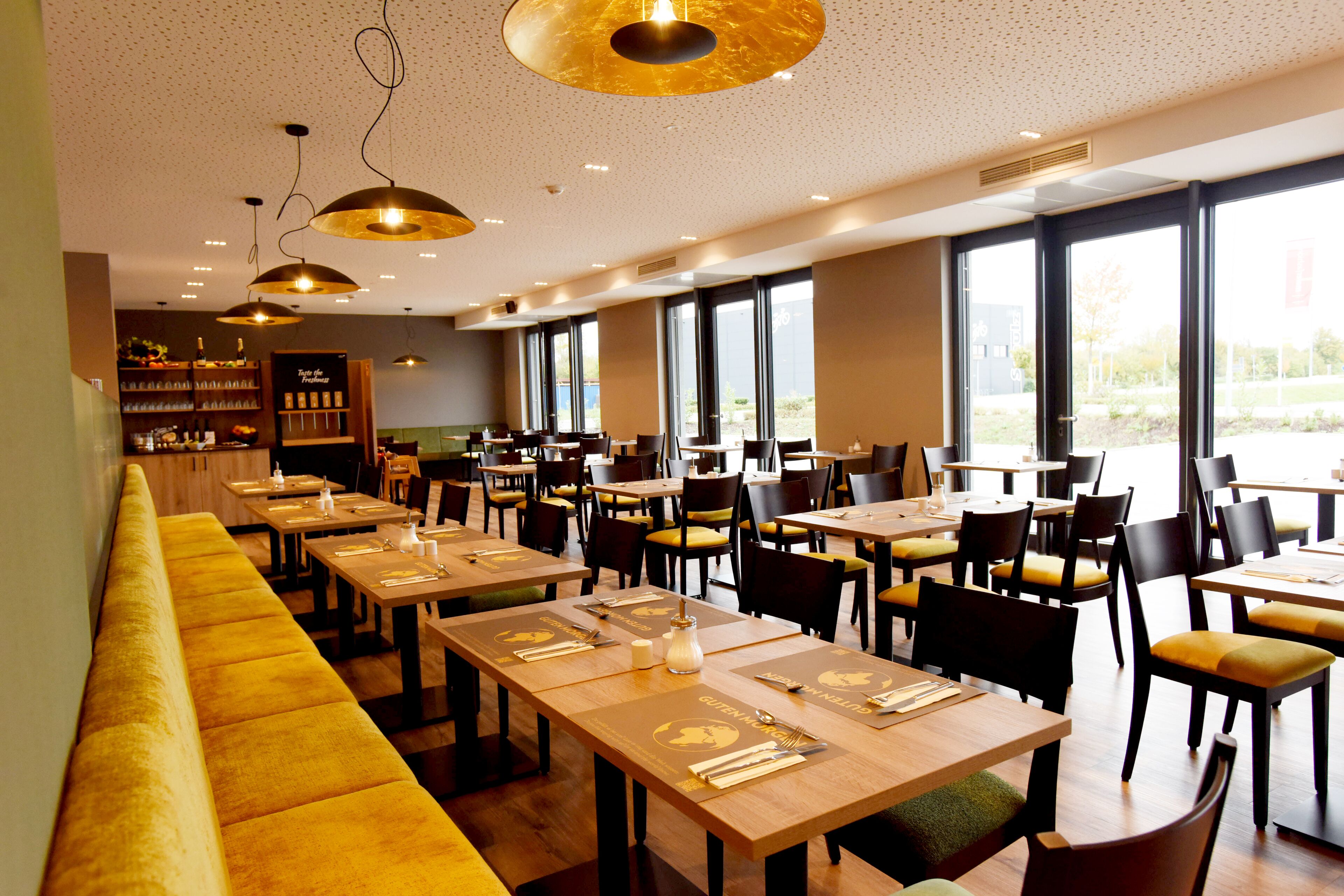 Un restaurante con largas mesas de madera, bancos acolchados de color amarillo y sillas negras.