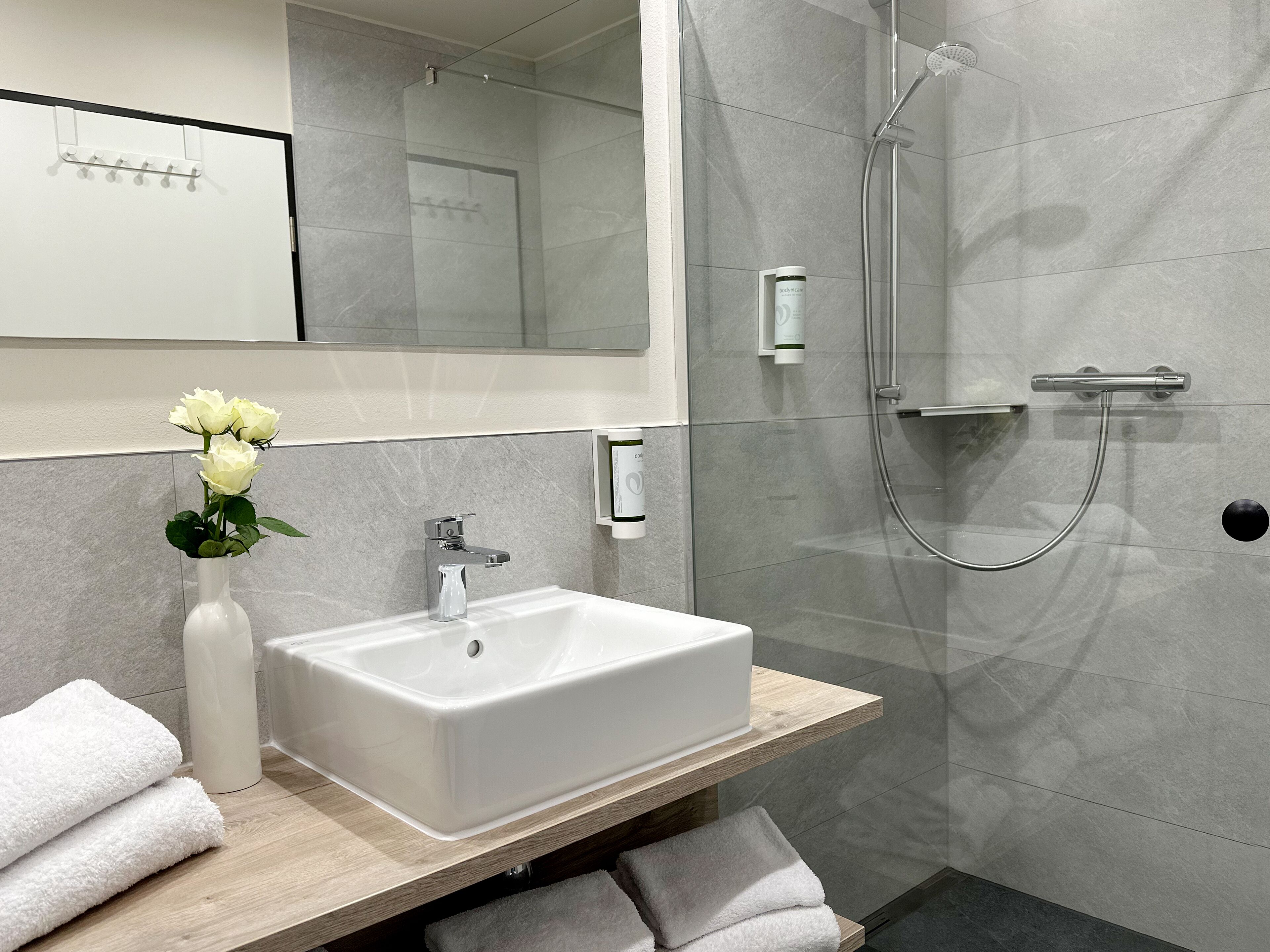 Un baño moderno con un lavabo blanco, una ducha y un espejo sobre el lavabo.