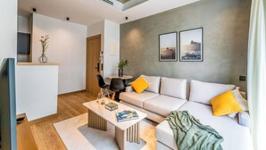 Una sala de estar moderna con un sofá, una mesa de centro y sillas. Hay una mesita con un florero y una planta. Dos cuadros están colgados en la pared.