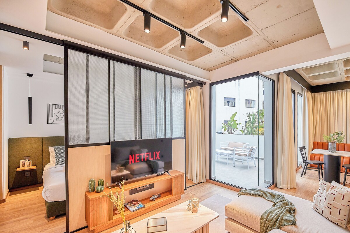 A modern living room with a large flat-screen TV, a sofa, a coffee table, and a dining area with a table and chairs.