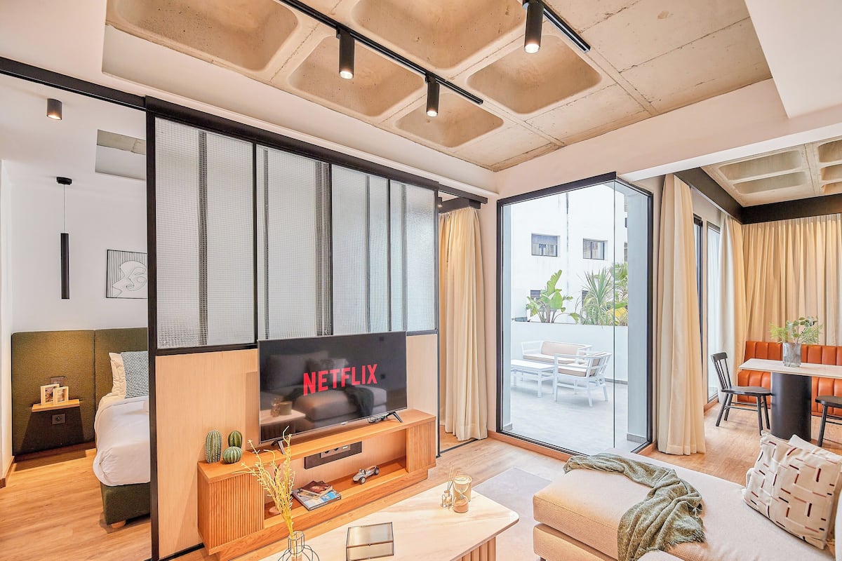 A modern living room with a large flat-screen TV, a sofa, a coffee table, and a dining area with a table and chairs.