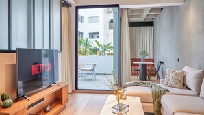 Una sala de estar moderna con un televisor de pantalla plana grande, un sofá, una mesa de centro y una zona de comedor con sillas.