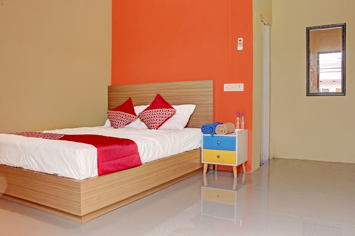 A modern hotel room with a wooden bed, red and white pillows, a blue and yellow nightstand, and a mirror on the wall.