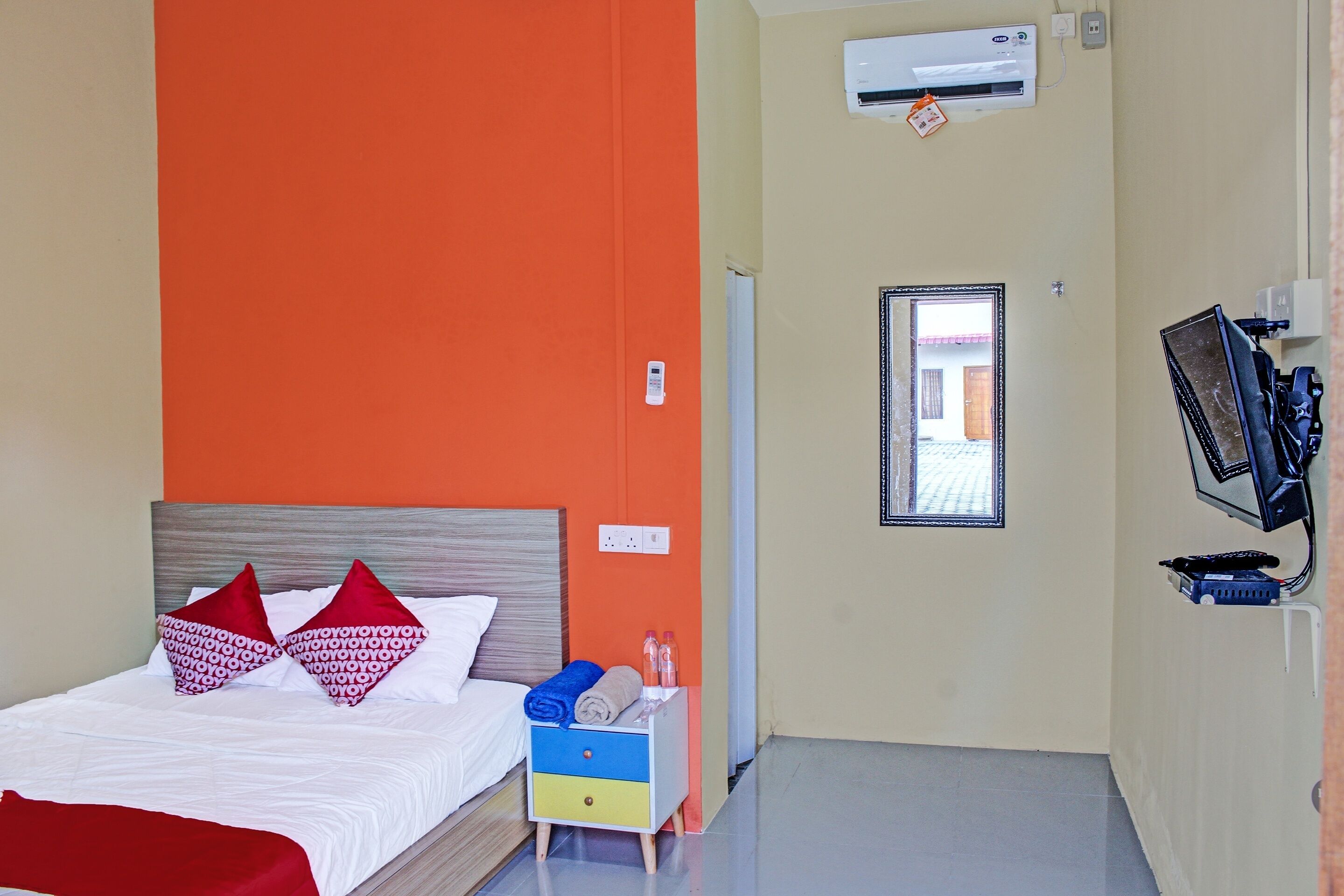 A hotel room with a bed, a nightstand, an air conditioning unit, a mirror, and a window.