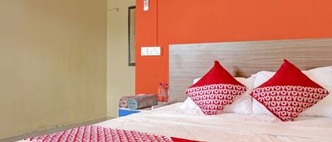 A hotel room with a bed, orange walls, and a red and white patterned bedspread.