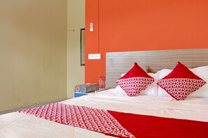 A hotel room with a bed, orange walls, and a red and white patterned bedspread.