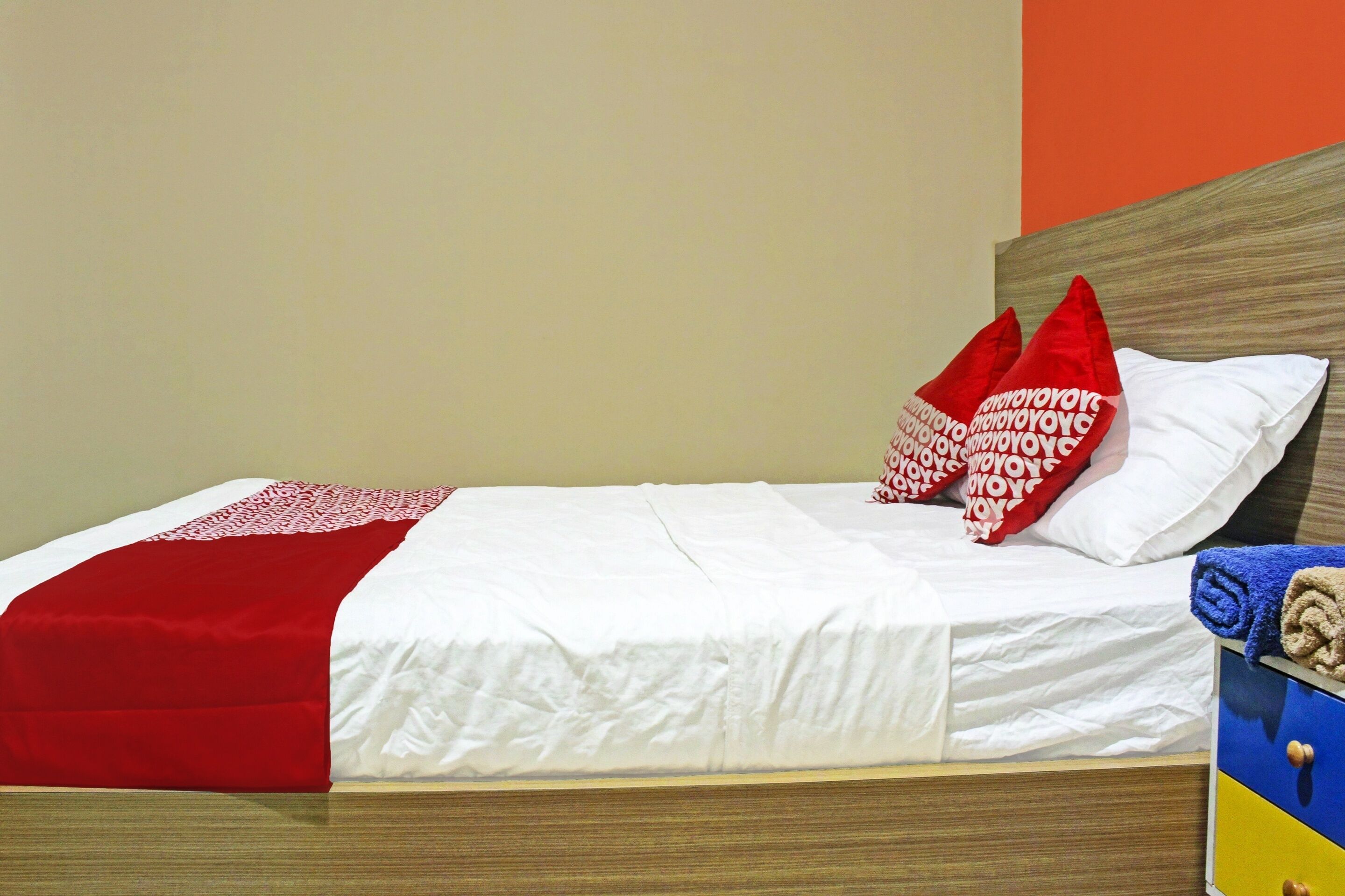 Cama com roupa de cama branca, travesseiros vermelhos e brancos, e manta vermelha.