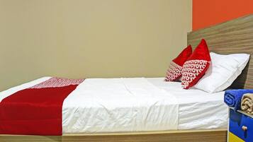 Cama com roupa de cama branca, travesseiros vermelhos e brancos, e manta vermelha.