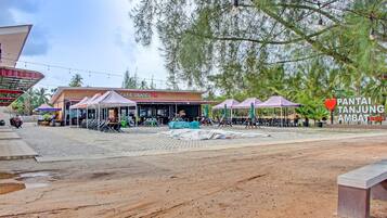 Una cafetería llamada 'CAFE DANIEL 76' con mesas al aire libre y un letrero que dice 'PANTAI TANJUNG AMBAT BEST'.