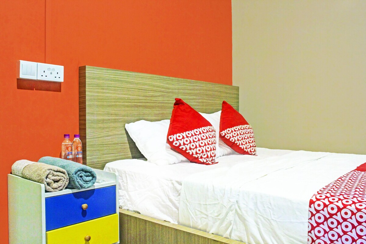 A hotel room with a bed, a nightstand with towels, and a wall socket.