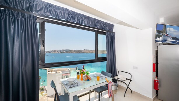 A balcony with a table set for two, overlooking a body of water. - Islet Promenade Studio with Hot Tub and Panoramic Sea Views by GetawaysMalta (St. Paul's Bay)