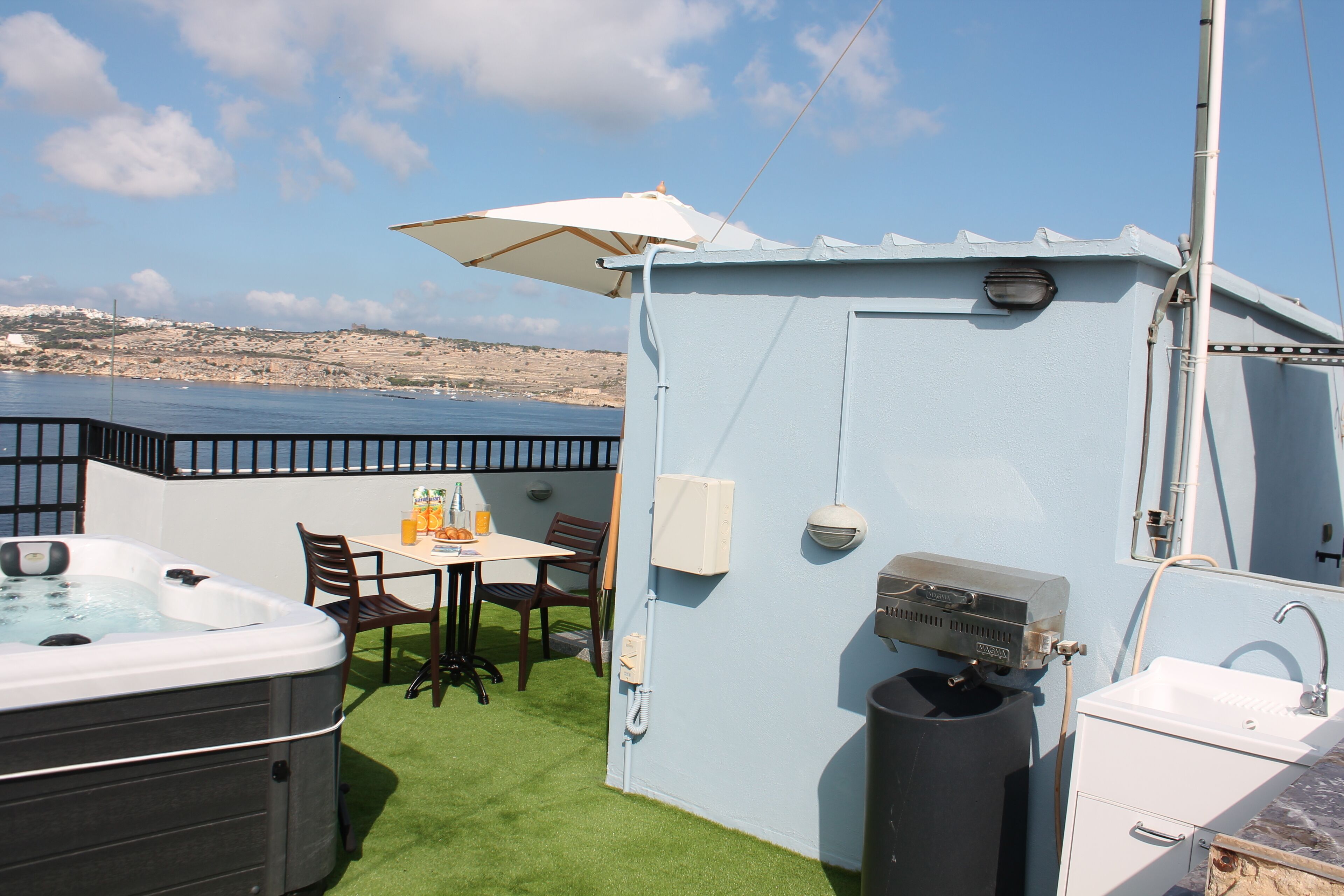 Een klein buitengebied met een jacuzzi, een tafel met stoelen, een witte wasbak en een grote parasol.