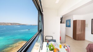 A balcony with a view of the sea, a dining table with breakfast items, and a wooden wardrobe. - Islet Promenade Studio with Hot Tub and Panoramic Sea Views by GetawaysMalta (St. Paul's Bay)