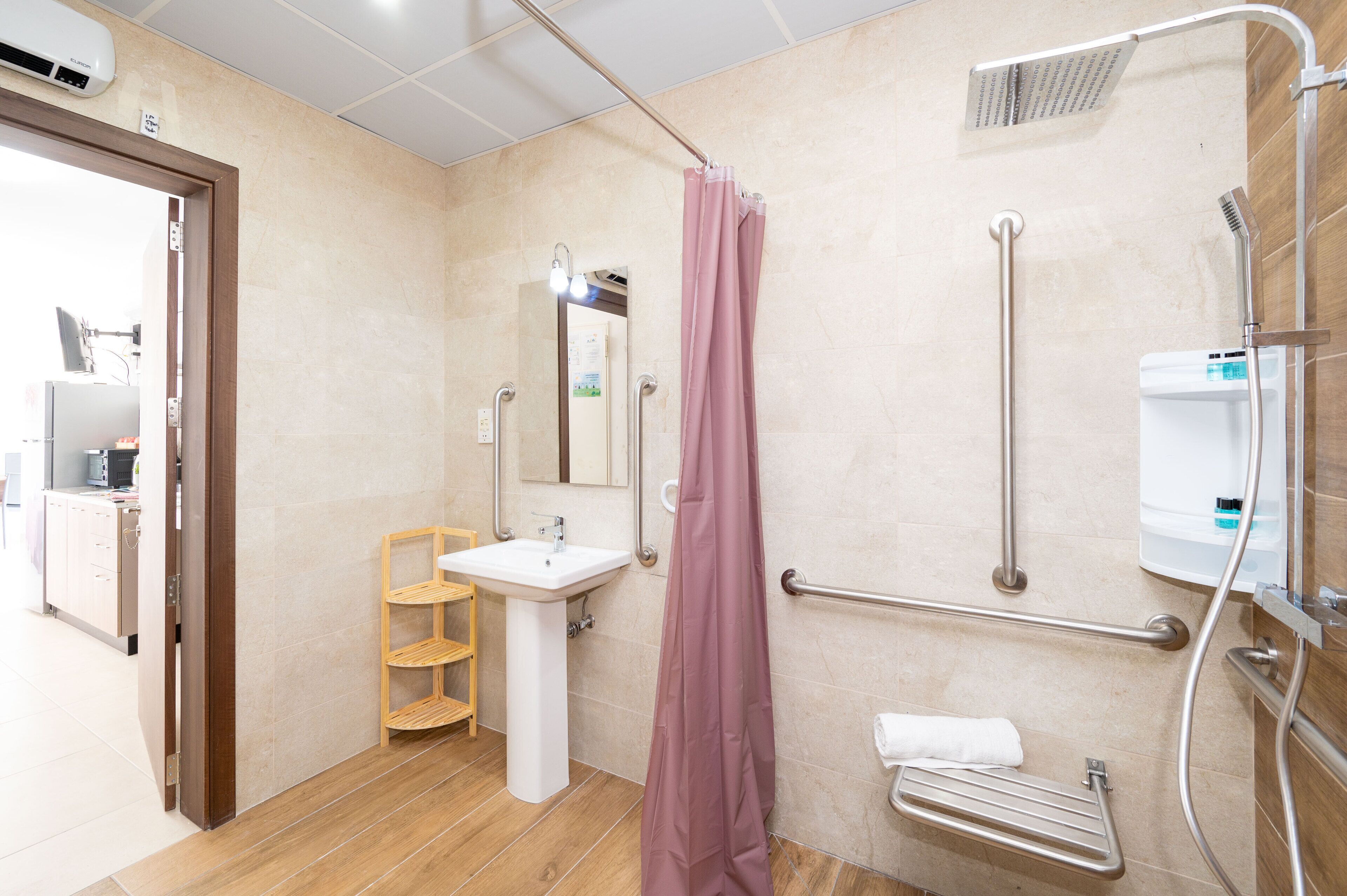 Een badkamer met wastafel, spiegel, douche en handgrepen.