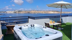 A hot tub with a table and chairs, an umbrella, and a view of the sea and buildings. - Islet Promenade Studio with Hot Tub and Panoramic Sea Views by GetawaysMalta (St. Paul's Bay)